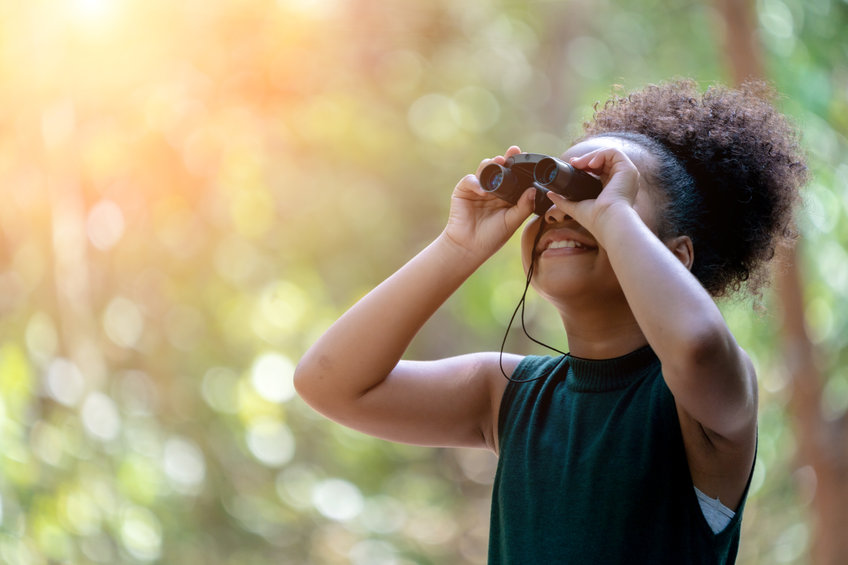 A girl looks into the sky with a pair of binoculars