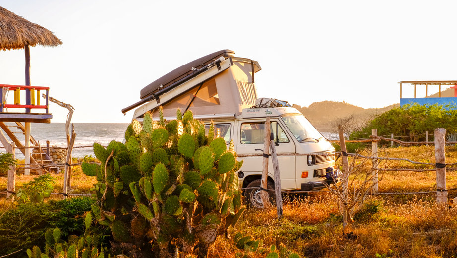 A westfalia camper van with the top up against a beach setting in Mexico