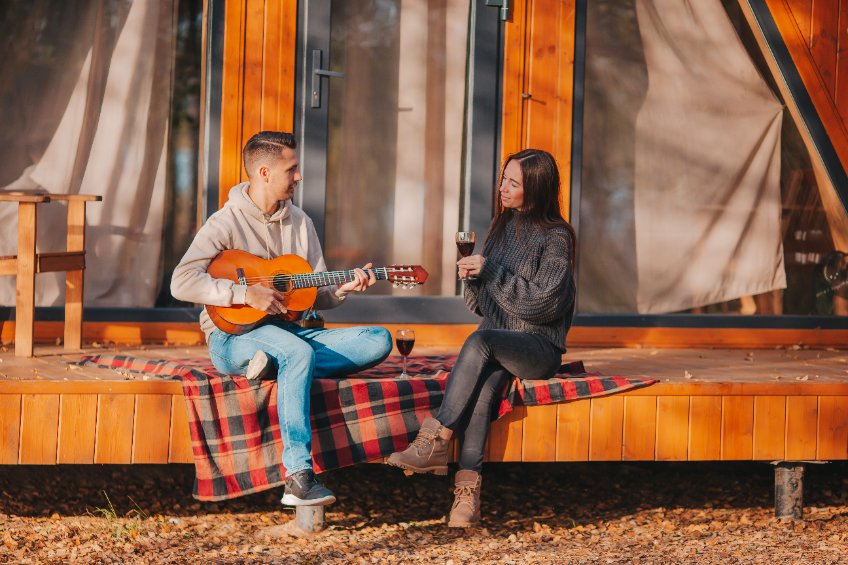 A man plays guitar to a woman siting on a wooden deck in Autumn.