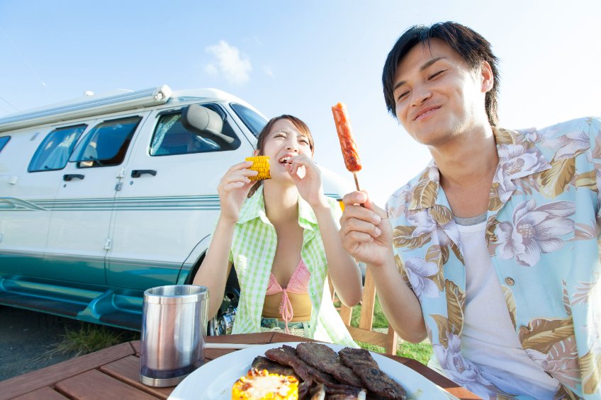 Two people in front of a campervan smilng and eating.
