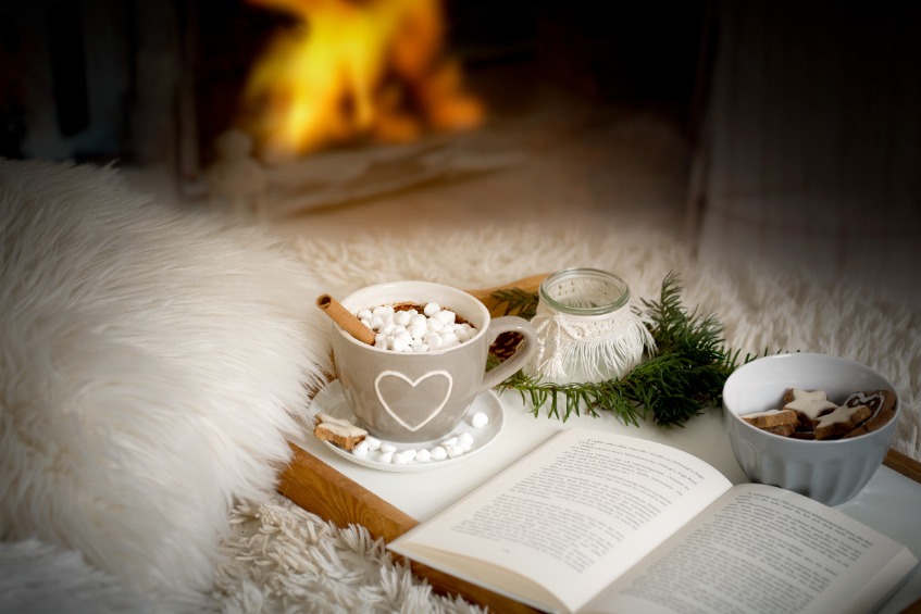A tray of hot chocolate and a book in front of a roaring fire.