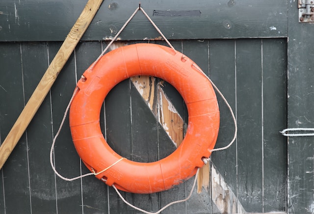 A life buoy roped against a wooden panel.